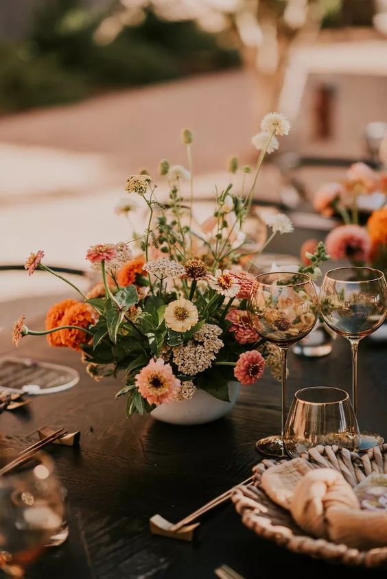 a colorful and textural wedding centerpiece of white and pink blooms, greenery and marigolds is a cool idea for summer or fall