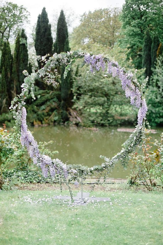 a pretty and delicate round wedding arch covered with eucalyptus and wisteria looks very lovely and very chic