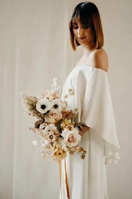 a lovely modern winter bridal outfit with an off the shoulder plain wedding dress plus a pastel wedding bouquet with grasses