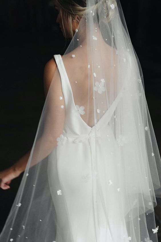 a modern plain wedding dress paired with a wedding veil embellished with smaller and bigger fabric flowers and beads