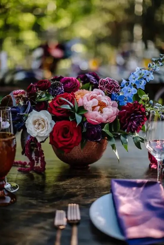 a chic jewel tone wedding centerpiece of deep red, blush, purple, burgundy and blue blooms and greenery is a lovely idea for the fall