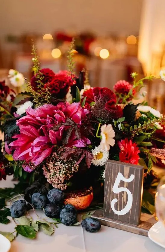 a dark pink and bold red lush floral centerpiece with grapes is a gorgeous decadent wedding centerpiece