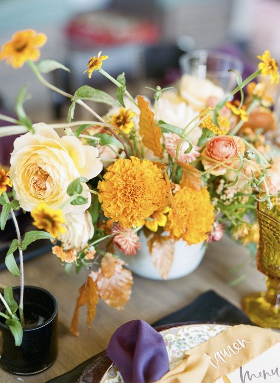 a fine art wedding centerpiece of peachy roses and ranunculus, marigolds, fall leaves and greenery is a catchy idea for the fall