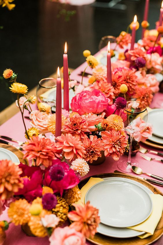 A jaw dropping and colorful wedding centerpiece of dahlias, marigolds, billy balls and other blooms, a pink table runner and gold placemats