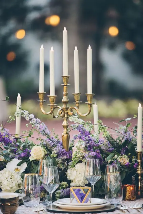 a beautiful wedding table setting with white hydrangeas and roses plus wisteria, candelabras, white porcelain and some favors