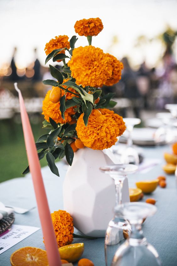 a modern wedding centerpiece of a faceted vase, marigolds and kumquat, plus citrus and marigolds on the table and bold candles