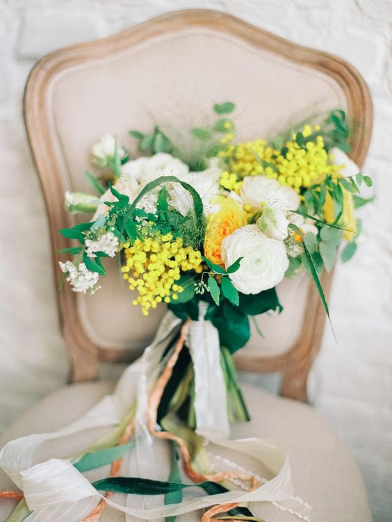 a whimsy spring wedding bouquet of white and yellow ranunculus, mimosa, white fillers and greenery is amazing and cute