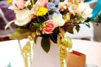 25 a bright summer wedding centerpiece of a book stack, a white metal jug, bright blooms and greenery and candles in blue jars
