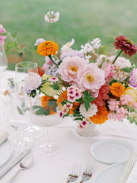a romantic wedding centerpiece of pink, blush, mauve and orange blooms including marigolds and with greenery