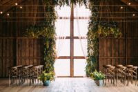 26  a rustic wedding ceremony space with a double-height window covered with mimosa as an arch, chandeliers and arrangements along the aisle