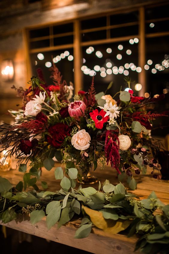 a bold wedding centerpiece of blush roses, red anemones, king proteas, greenery and amaranthus is a very chic idea for the fall