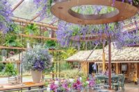 27 a colorful wedding reception space with chandeliers covered with wisteria and greenery, bold blooms on the table and a large planter with blooms