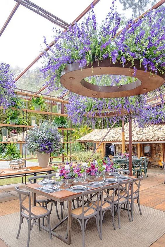 a colorful wedding reception space with chandeliers covered with wisteria and greenery, bold blooms on the table and a large planter with blooms