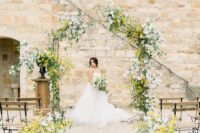27 a vivacious spring wedding ceremony space with an arch done with mimosa, greenery and some white blooms and arrangements lining up the aisle