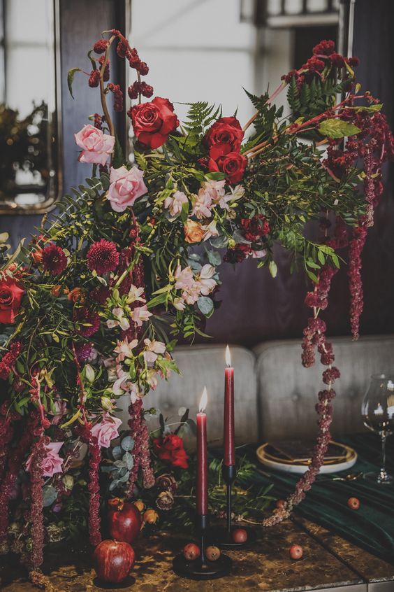 a bold wedding centerpiece of blush and red roses, mums, greenery and amaranthus plus burgundy candles