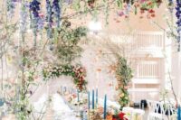 28 a colorful wedding reception space with wisteria, roses, peonies and greenery arches over the table, colorful blooms and blue candles