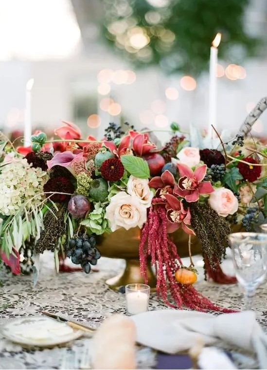 a lush and colorful fall wedding centerpiece of pink, mauve, burgundy, blush blooms, greenery and grapes plus a feather