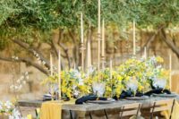 29 a beautiful spring wedding tablescape with a table of concrete, mimosa and cherry blossom, a yellow runner, black napkins and tall and thin candles