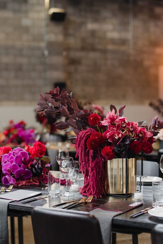 a bold wedding centerpiece of amaranthus, dark foliage, red mumes, pink lilies and a shiny gold vase