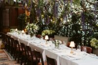 29 a cozy and dreamy wedding reception space with wisteria hanging down and greenery, a long table and table lamps plus leather chairs