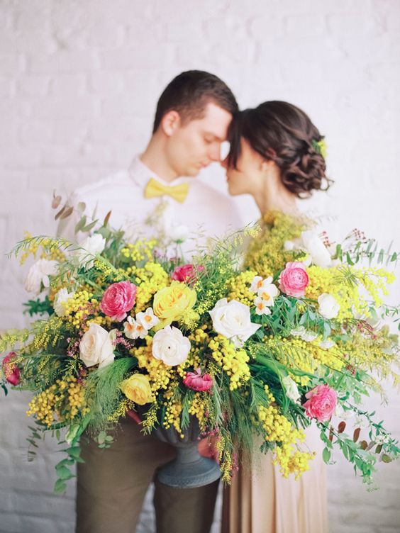 a bright and lush spring wedding centerpiece of blush and pink raunuculus, mimosa and greenery is jaw-dropping