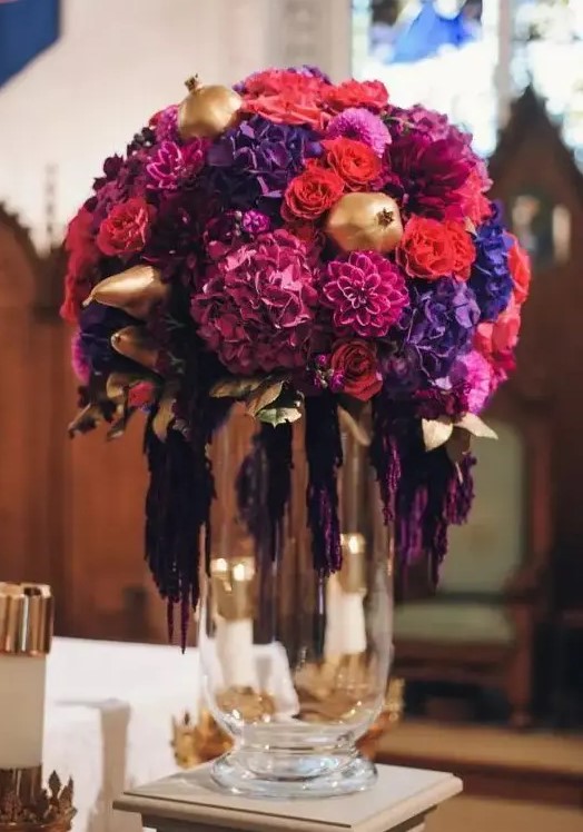 a fantastic lush wedding centerpiece of purple, violet, fuchsia, orange blooms and gilded pears and pomegranates is wow