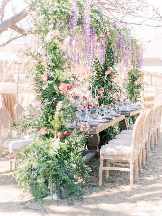 a dreamy wedding reception space covered with greenery, pink and fuchsia blooms and wisteria hanging down is amazing