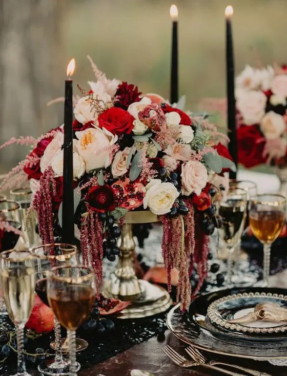 a lush moody wedding centerpiece of blush and red blooms, dark grapes and pomegranates plus black candles