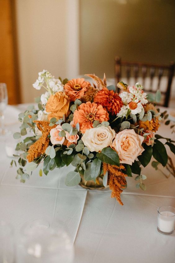 a wedding centerpiece of blush roses, marigolds, mumes, white fillers and greenery is a cool and bright idea