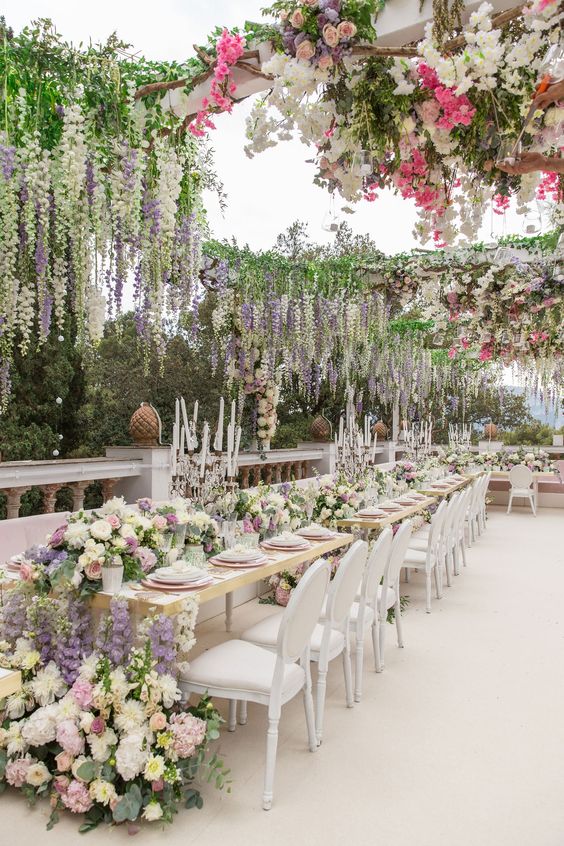 a fabulous outdoor flower-filled wedding reception space done with lots of peachy, lilac, pink, white blooms including wisteria and greenery