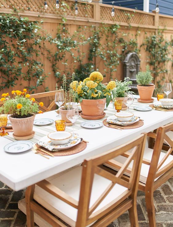 a welcoming rustic wedding tablescape with woven mats, potted marigolds and dahlias, amber glasses and some printed porcelain