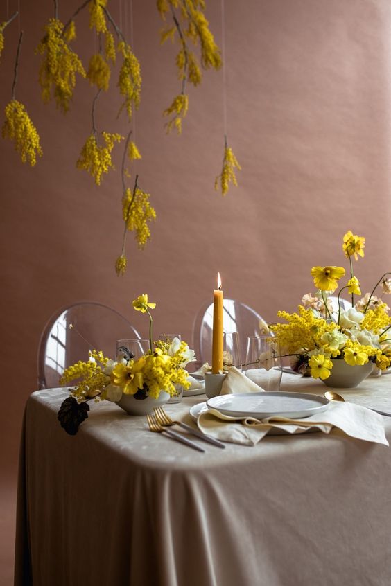 a fine art wedding tablescape with a grey tablecloth and napkins, yellow centerpieces with mimosa and some mimosa over the table