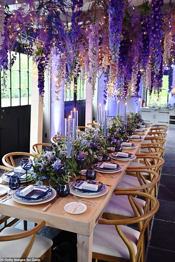 a gorgeous bold wedding reception space with wisteria hanging down, with greenery and bold purple blooms on the table, violet porcelain and lilac candles