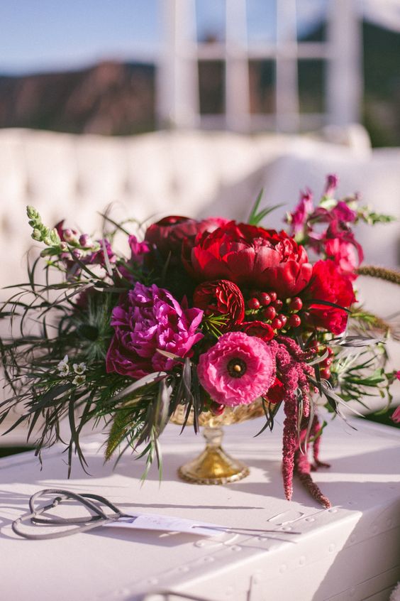 a bold wedding centerpiece of red and pink peonies, anemones, greenery, berries and amaranthus is amazing