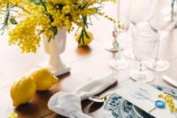 35 a fun wedding tablescape with a mimosa centerpiece, blue and white porcelain, a white napkin, glasses and lemons on the table