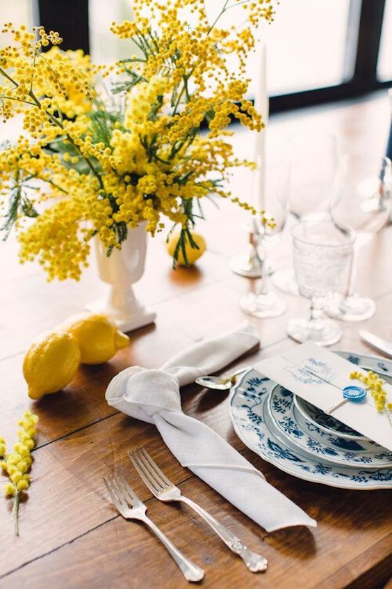 a fun wedding tablescape with a mimosa centerpiece, blue and white porcelain, a white napkin, glasses and lemons on the table