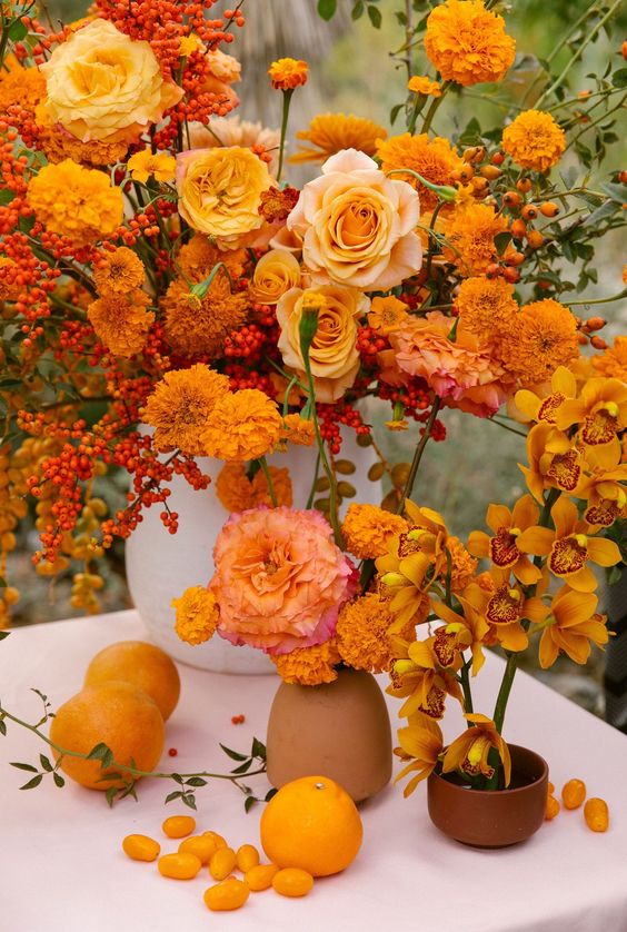 an oversized fall wedding centerpiece of berries, roses and marigolds, a marigold arrangement and an orchid one