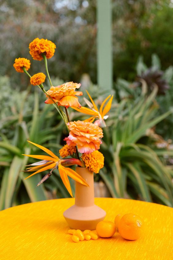 a modern tropical wedding centerpiece of a terracotta vase, marigolds and tropical blooms and citrus on the table