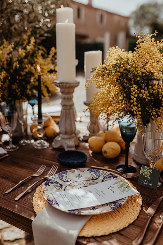 a Mediterranean wedding tablescape with mimosa centerpieces, pillar candles, lemons on the table, woven placemats and printed porcelain