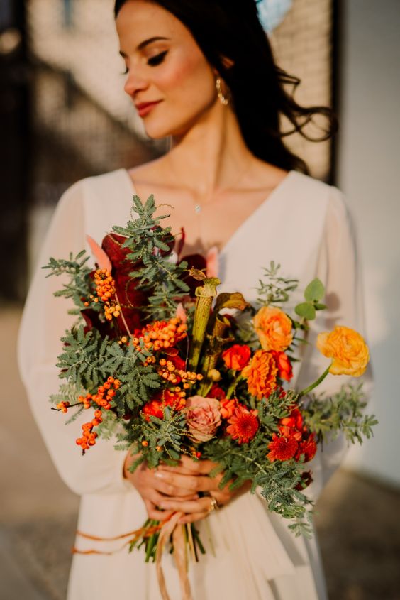 a bold fall wedding bouquet of marigolds, burgundy and peachy blooms, berries, greenery and large leaves is a unique idea