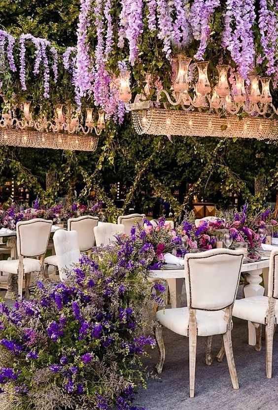 a luxurious and sophisticated wedding reception space with chandeliers with wisteria, a lush wedding table runner with purple blooms and greenery