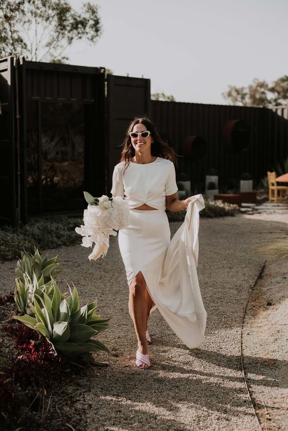 a modern wedding separate with a knotted crop top with short sleeves and a maxi skirt with a front slirt plus pink mules