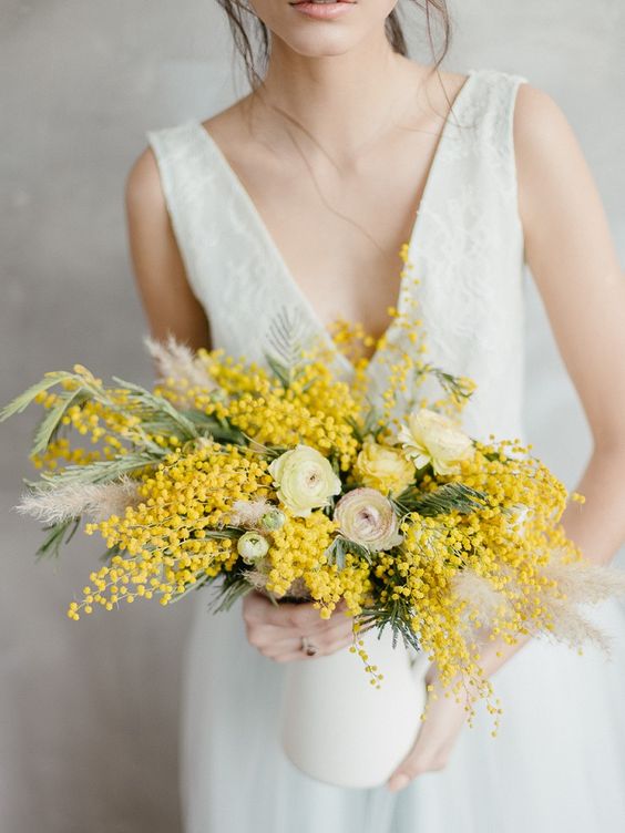 a pretty wedding centerpiece with ranunculus, mimosa and pampas grass is a lovely idea for a spring wedding
