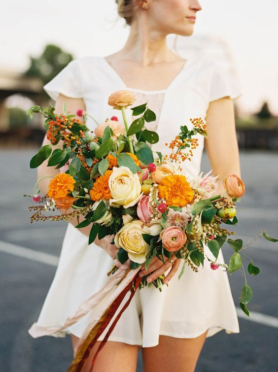 a bold wedding bouquet of pale yellow roses and ranunculus, greenery, berries and leaves plus long ribbon is a cool idea for a summer or fall bride