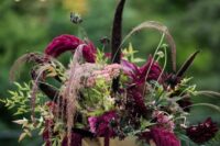 41 a sophisticated moody wedding centerpiece of greenery, burgundy dahlias and anemones, feathers, grasses and amaranthus