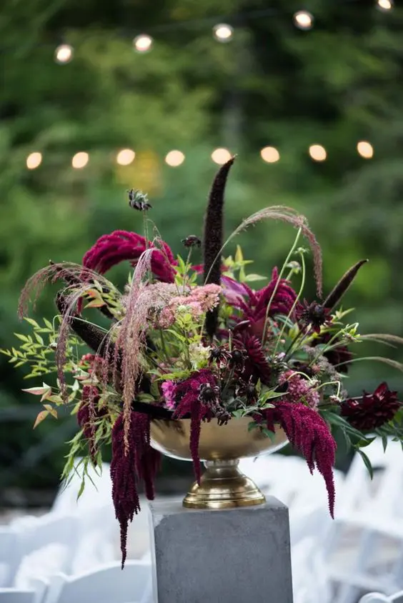 a sophisticated moody wedding centerpiece of greenery, burgundy dahlias and anemones, feathers, grasses and amaranthus