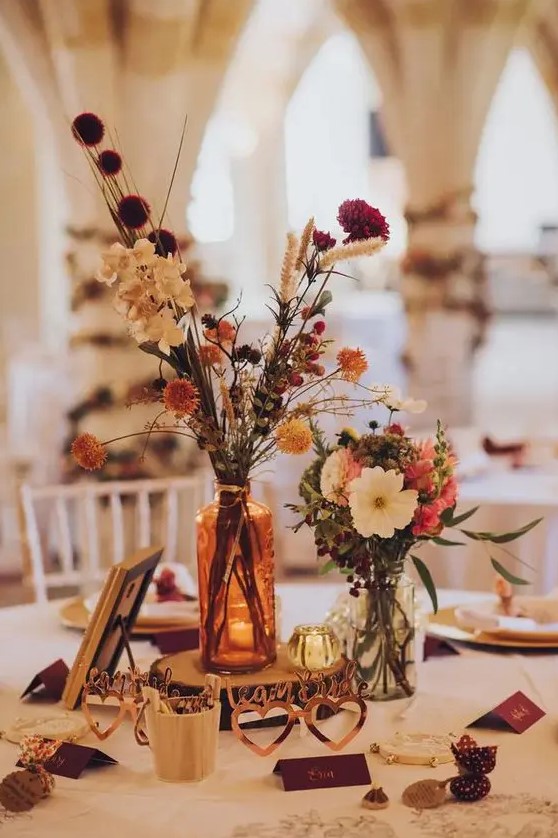 pretty and bright fall boho wedding centerpiece of white, pink, red, rust dried blooms, greenery, a wood slice and candleholders