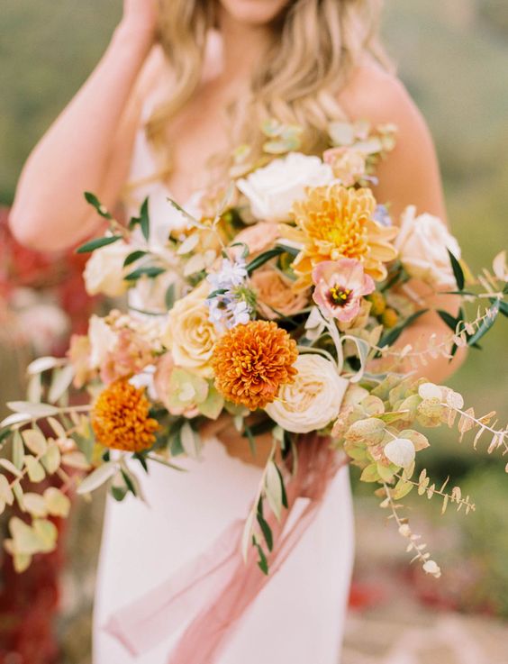 a bright and lush wedding bouquet of marigolds, neutral roses and pink tulips, with textural greenery for a summer or fall wedding