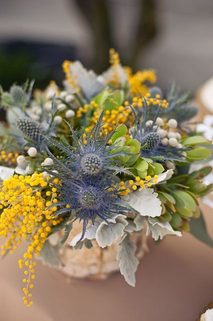 a rustic wedding centerpiece with pale leaves, mimosa, thistles, greenery and berries is a cool and cozy idea for a rustic wedding