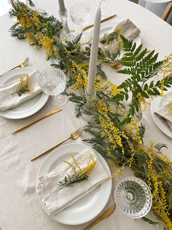 a spring wedding tablescape in neutrals, with a mimosa runner and white porcelain, neutral textiles and tall and thin candles